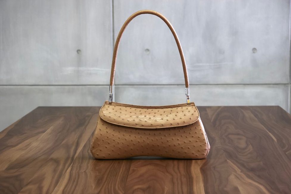 strukturierte cognacfarbene Ledertasche mit goldenem Verschluss auf hellem Schreibtisch